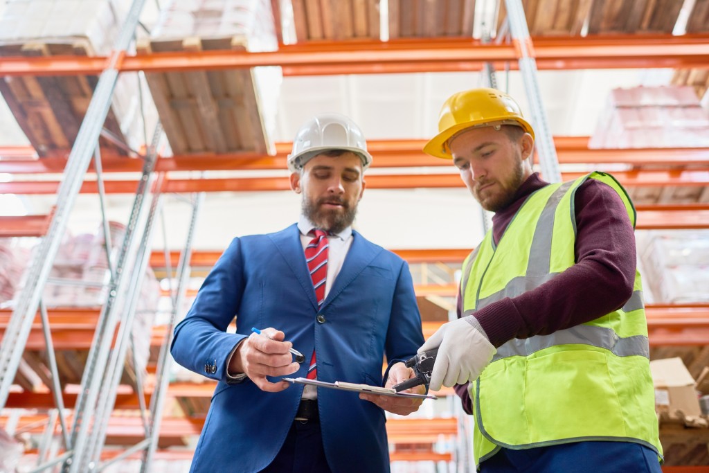 Waist up portrait of mature businessman talking to warehouse worker, discussing inventory on clipboard